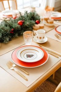 Alright, here’s your holiday table: Christmas-y plates, gold cutlery that thinks it's royalty, and a centerpiece showing off pine branches like it’s in a winter pageant.