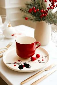Alright, here's the scoop: festive table vibes with a red cup nestled on a plate, all spruced up with holly. Oh, and the vase? Basically Santa's botanical garden.