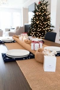 Imagine a dining table that said, 'I'm here to party' featuring plates ready for feasts, wrapped gifts to distract from those burnt pies, and a burlap runner saying rustic chic. Candles are vibing for mood lighting while the Christmas tree photobombs in the background.