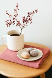 A white mug of tea with berries? Fancy! And hey, three powdered doughnuts on a pink cloth—because who needs calorie counting when your table's this cute?