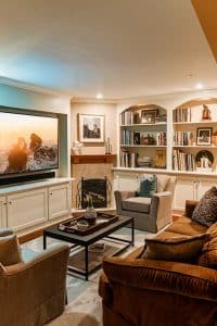 Step into Sofa Kingdom: oversized TV vying for attention against the roaring fireplace, while bookshelves whisper wisdom beside comfy armchairs. Cozy chaos wins!.