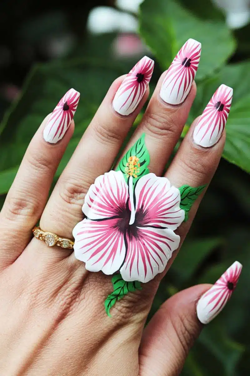 Lets talk about this hand, starring nails with a flower power moment. That middle finger hibiscus screams Im on vacation, matched with a gold ring for extra flair against lush green leaves.