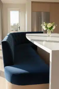 Curved navy bench cozies up to a white kitchen counter—because your snacks deserve better seating than you do. Bonus: flowers just for show.